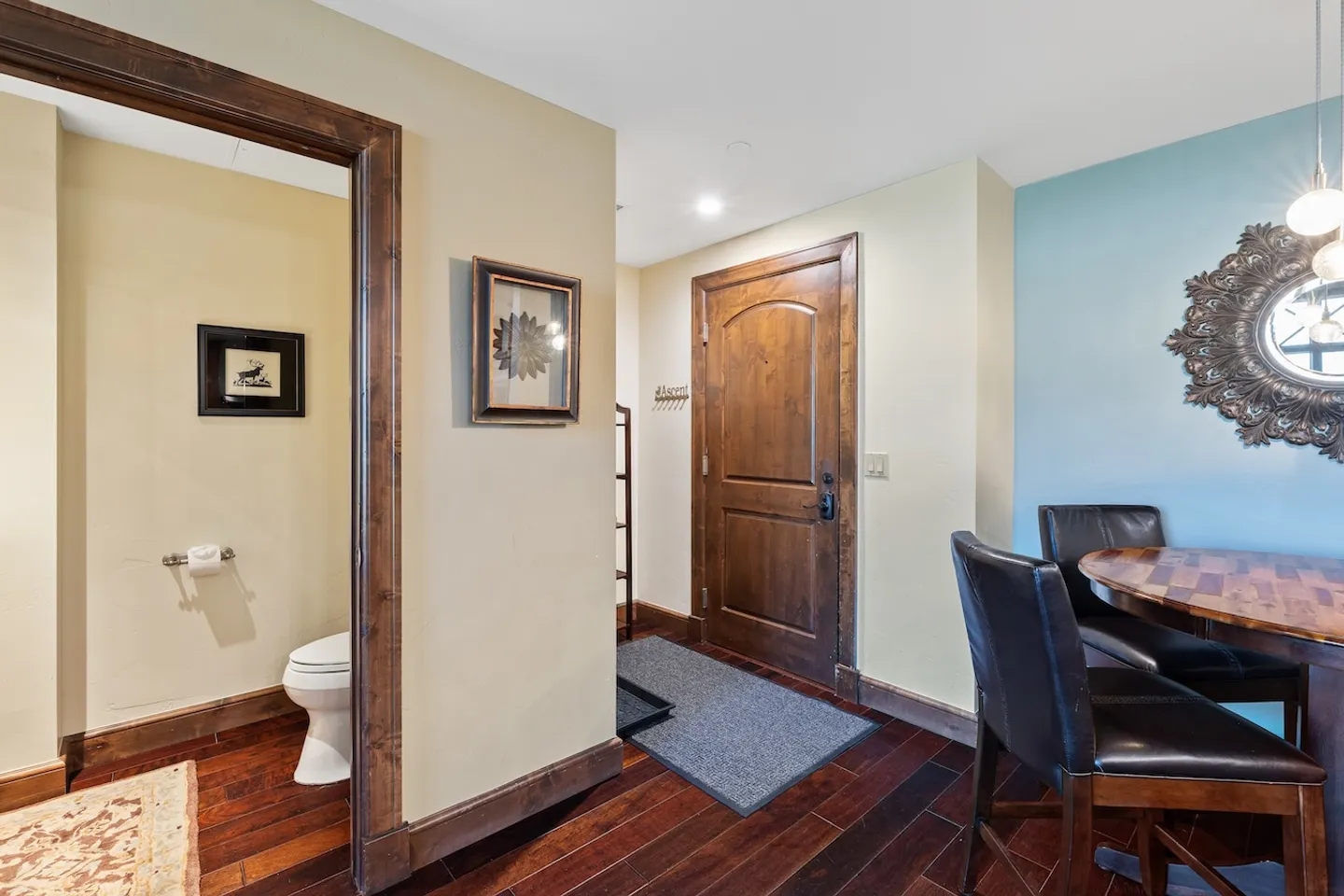 Entryway with a wooden front door, dark wood flooring, an adjacent half bathroom, and a dining table with leather chairs.