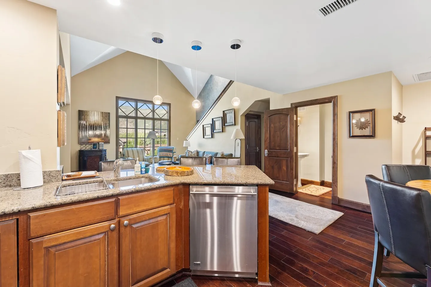 Kitchen island with granite countertop and stainless steel dishwasher looking toward an open living area and entryway.