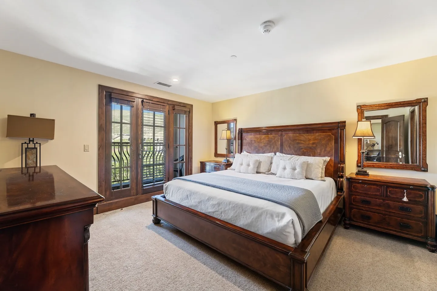 Bedroom featuring a wooden bed frame, matching nightstands with mirrors, a dresser, and glass French doors leading to an outdoor balcony.