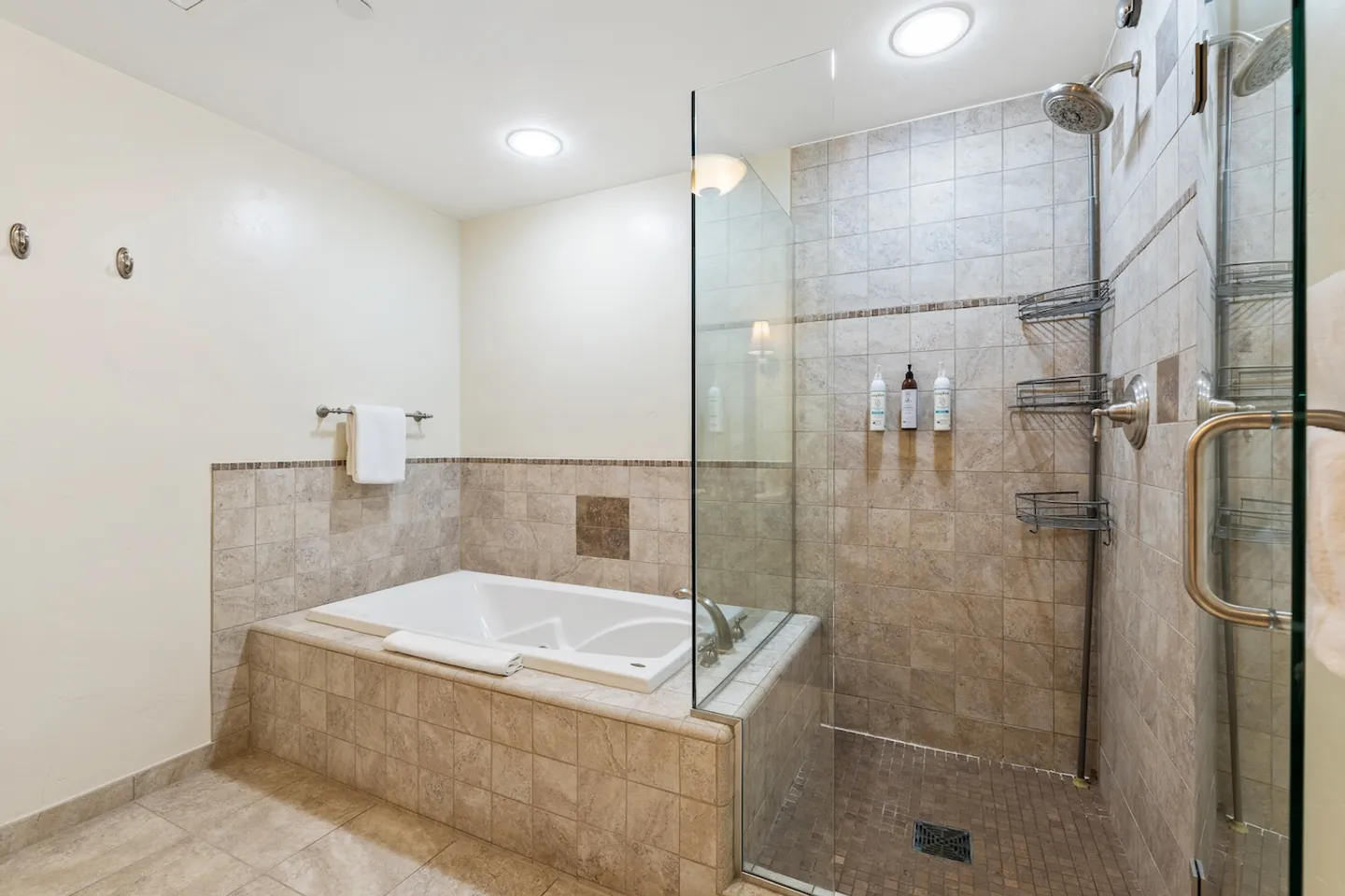 Bathroom with a tiled soaking bathtub beside a glass-enclosed walk-in shower with tile walls.