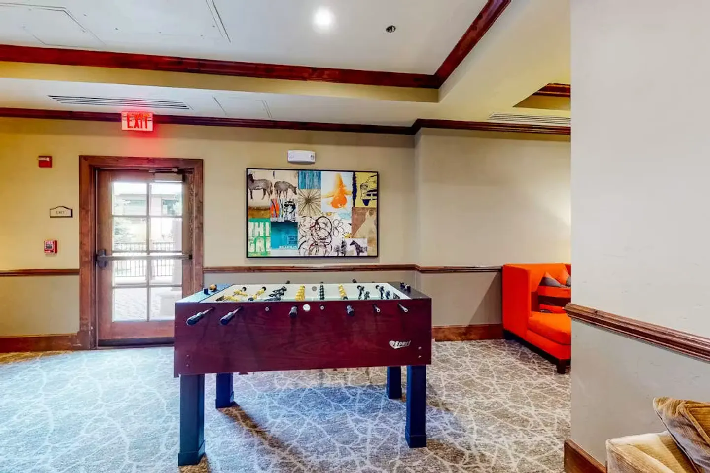 Recreation area featuring a foosball table centered on patterned carpet near an exit door.