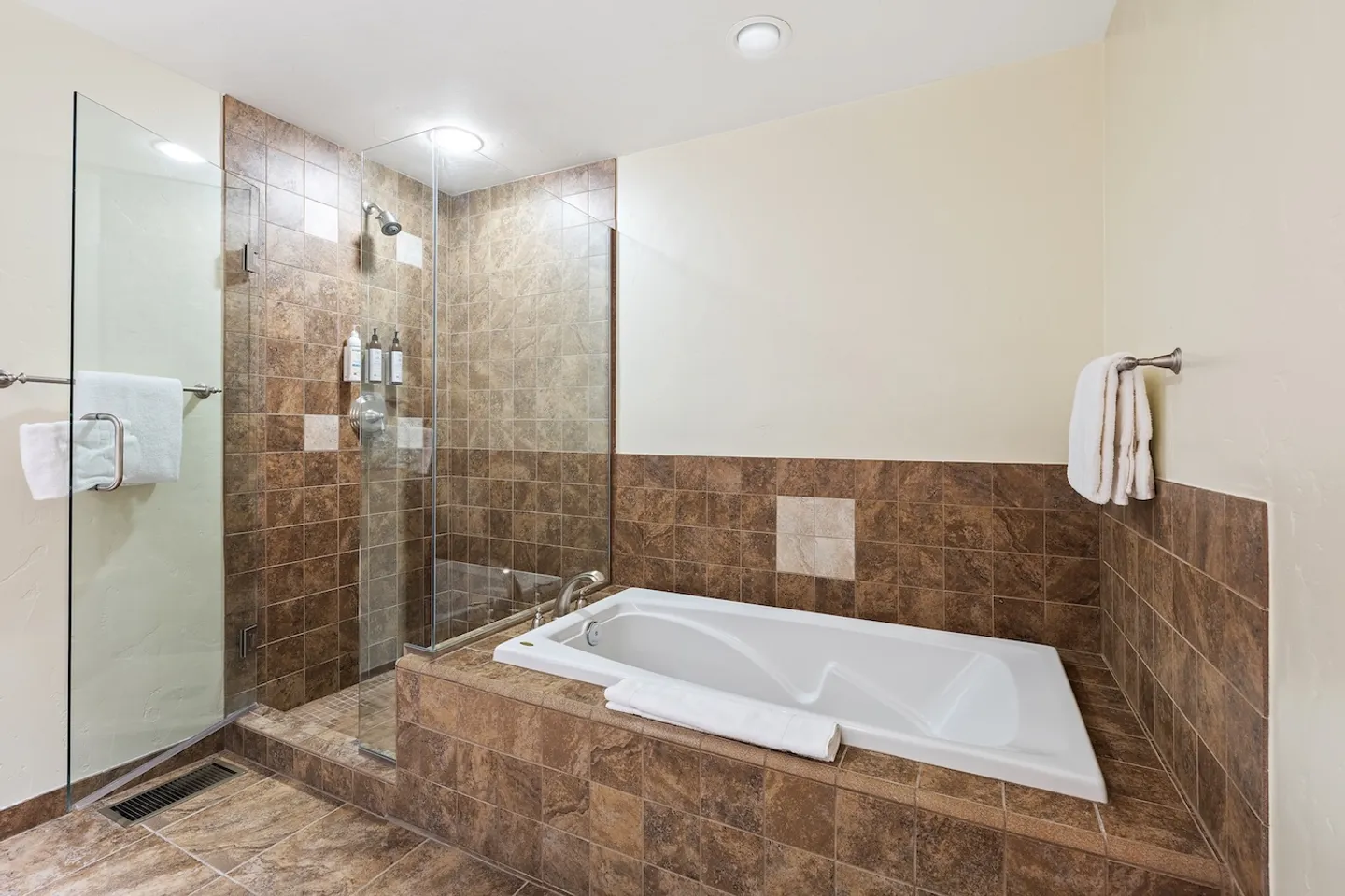 Bathroom featuring a drop-in bathtub surrounded by brown tile and an adjacent walk-in glass shower enclosure.