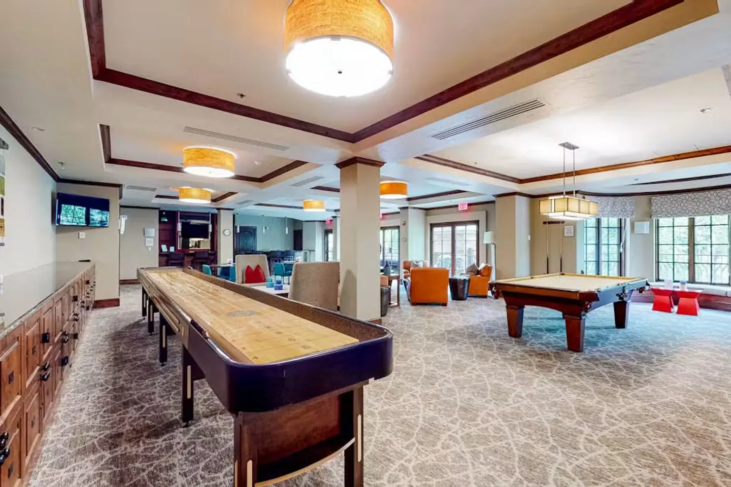 Game room featuring a long shuffleboard table, a pool table, patterned carpeting, and warm ceiling light fixtures.