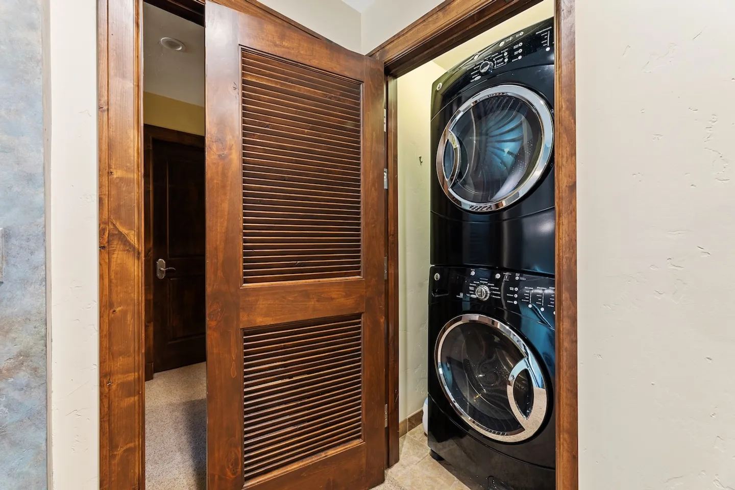 Open louvered wooden closet door revealing a stacked black washer and dryer set.