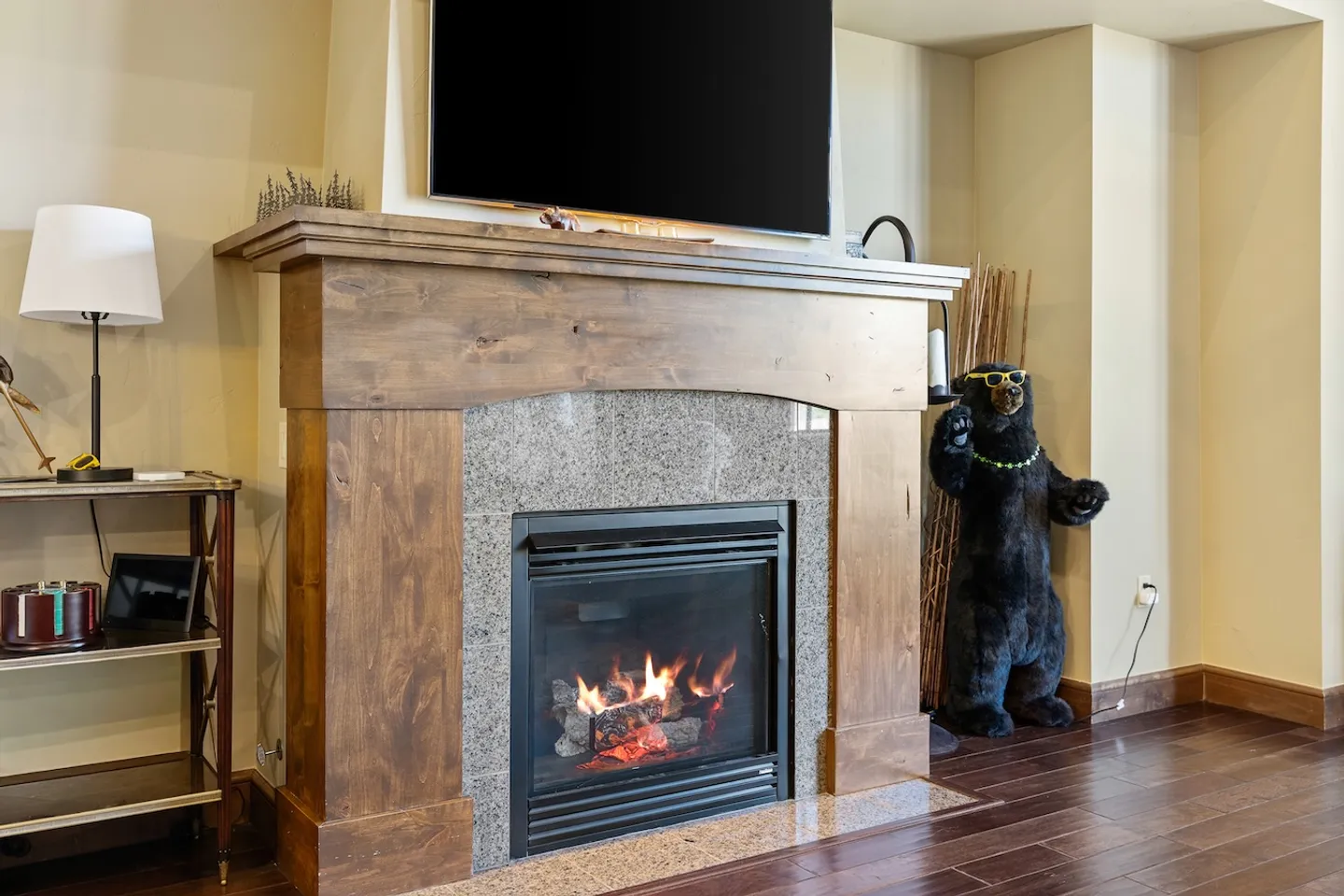 Lit gas fireplace surrounded by speckled granite and a rustic wood mantel beneath a wall-mounted flat-screen television.