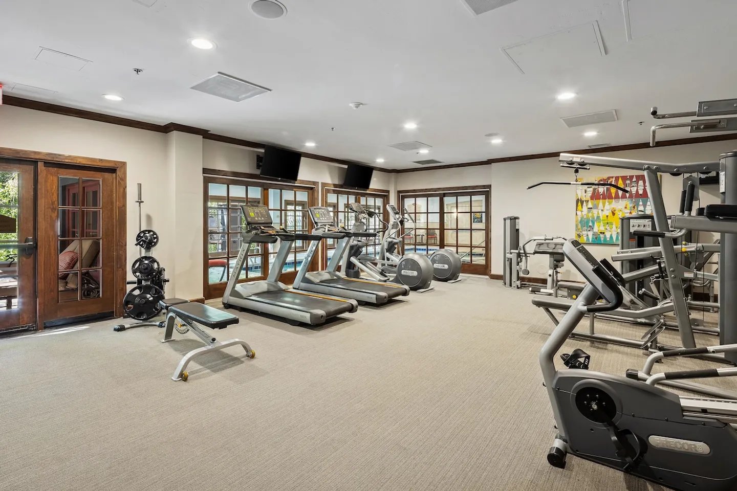 Indoor fitness center with carpeted floor, treadmills, elliptical machines, weight bench, and strength training equipment.