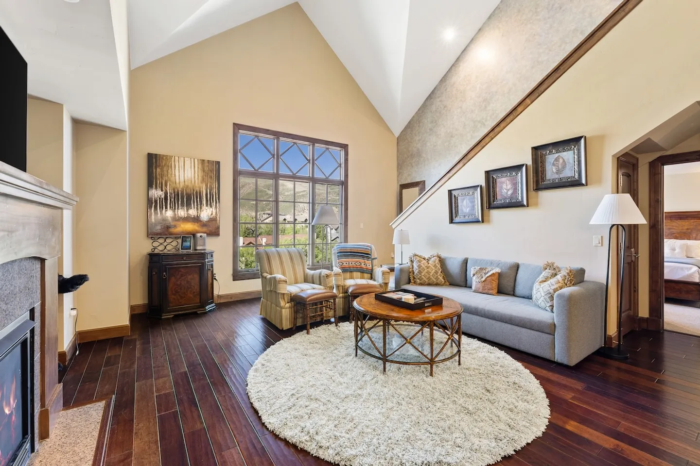 Living room with vaulted ceilings, hardwood floors, a gray sofa, armchairs, a round coffee table, and a large window.
