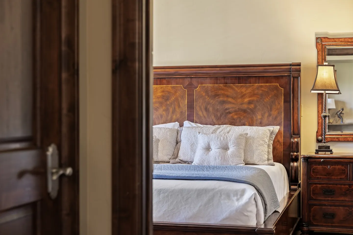 A partially open wooden doorway looking into a bedroom with an ornate wooden bed and nightstand.