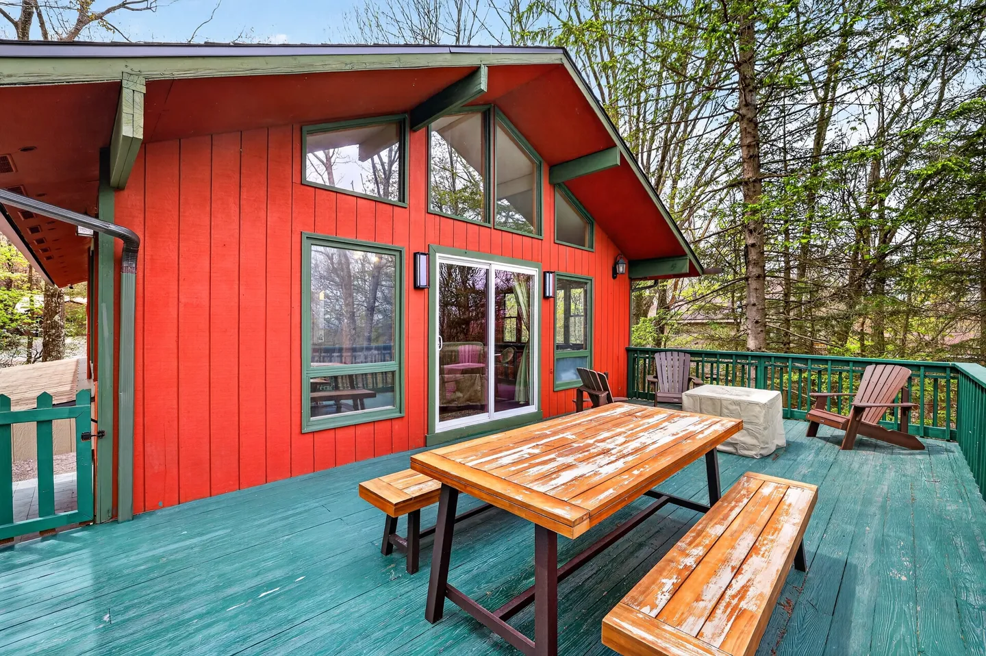 Spacious green wooden deck with a picnic table and outdoor seating outside a red wooden house with large windows.