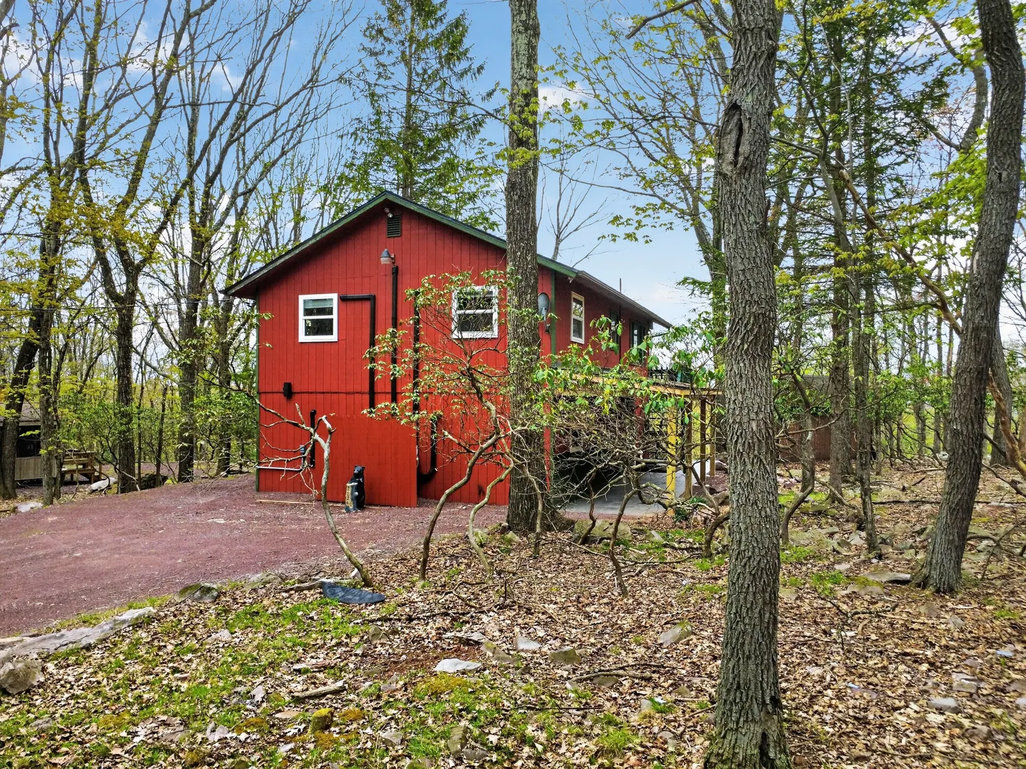 Exterior of a red two-story house nestled among tall trees with a gravel driveway.
