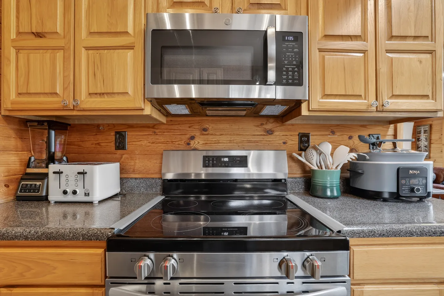 Kitchen counter area with an electric range, over-the-range microwave, wood cabinets, and small countertop appliances.