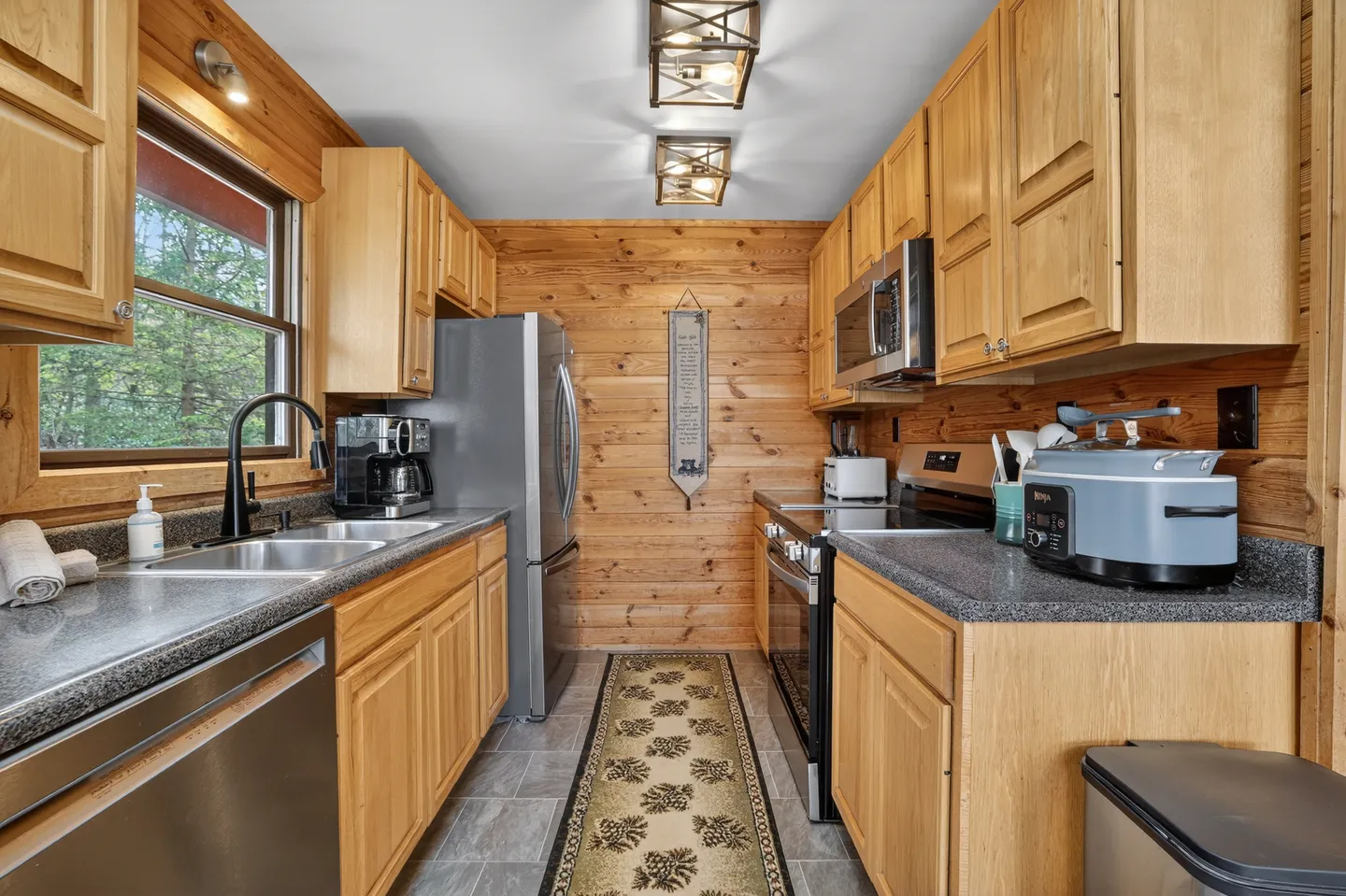Galley kitchen with wood-paneled walls, wooden cabinetry, dark countertops, and stainless steel appliances.