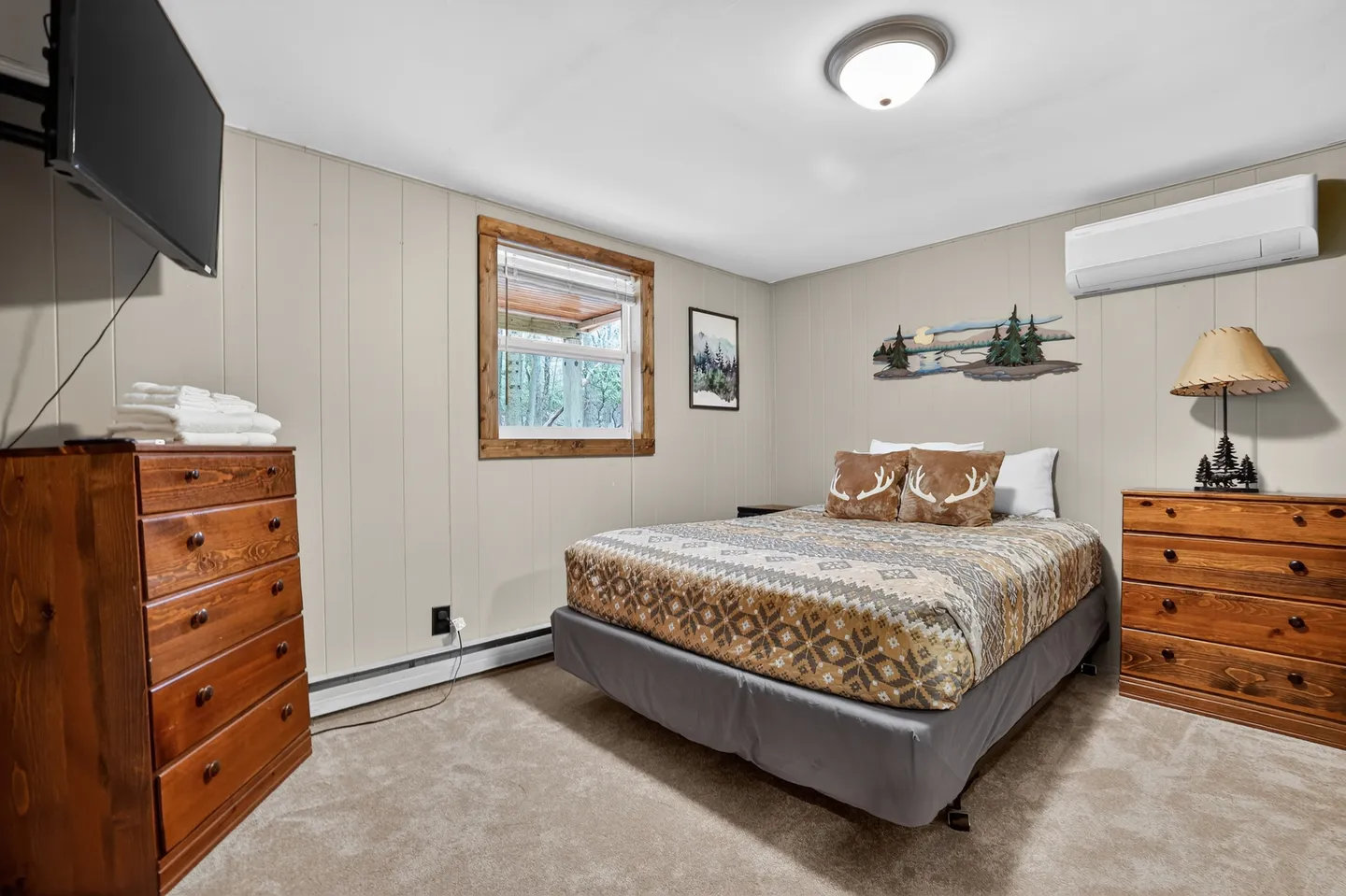 Bedroom featuring a made bed with a patterned comforter, two wooden dressers, a wall-mounted TV, and an air conditioning unit.