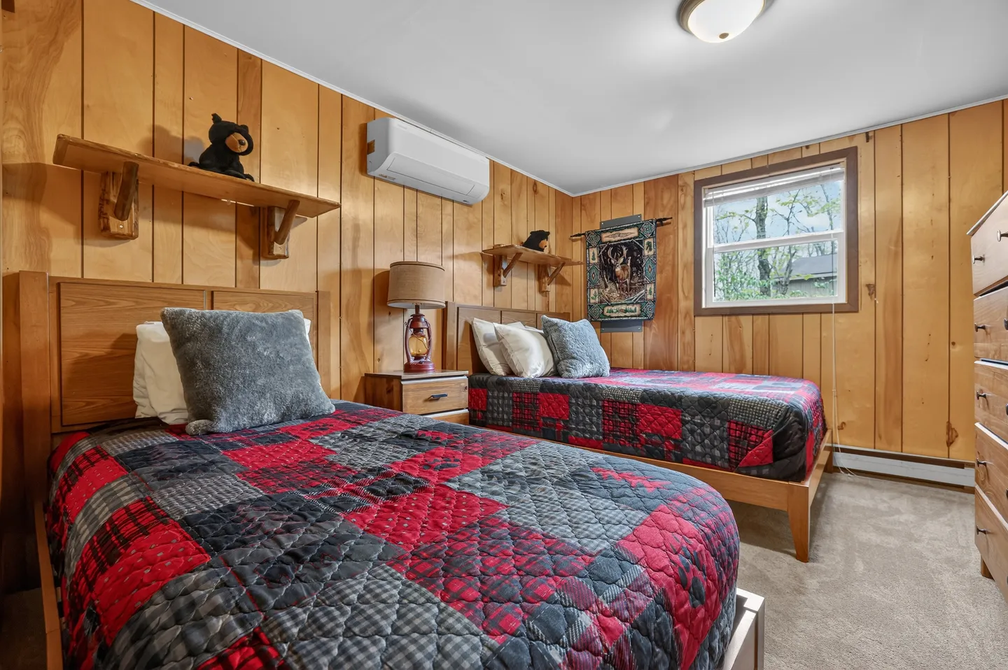 Bedroom with two twin beds featuring red and black plaid quilts, wood paneled walls, and carpet flooring.
