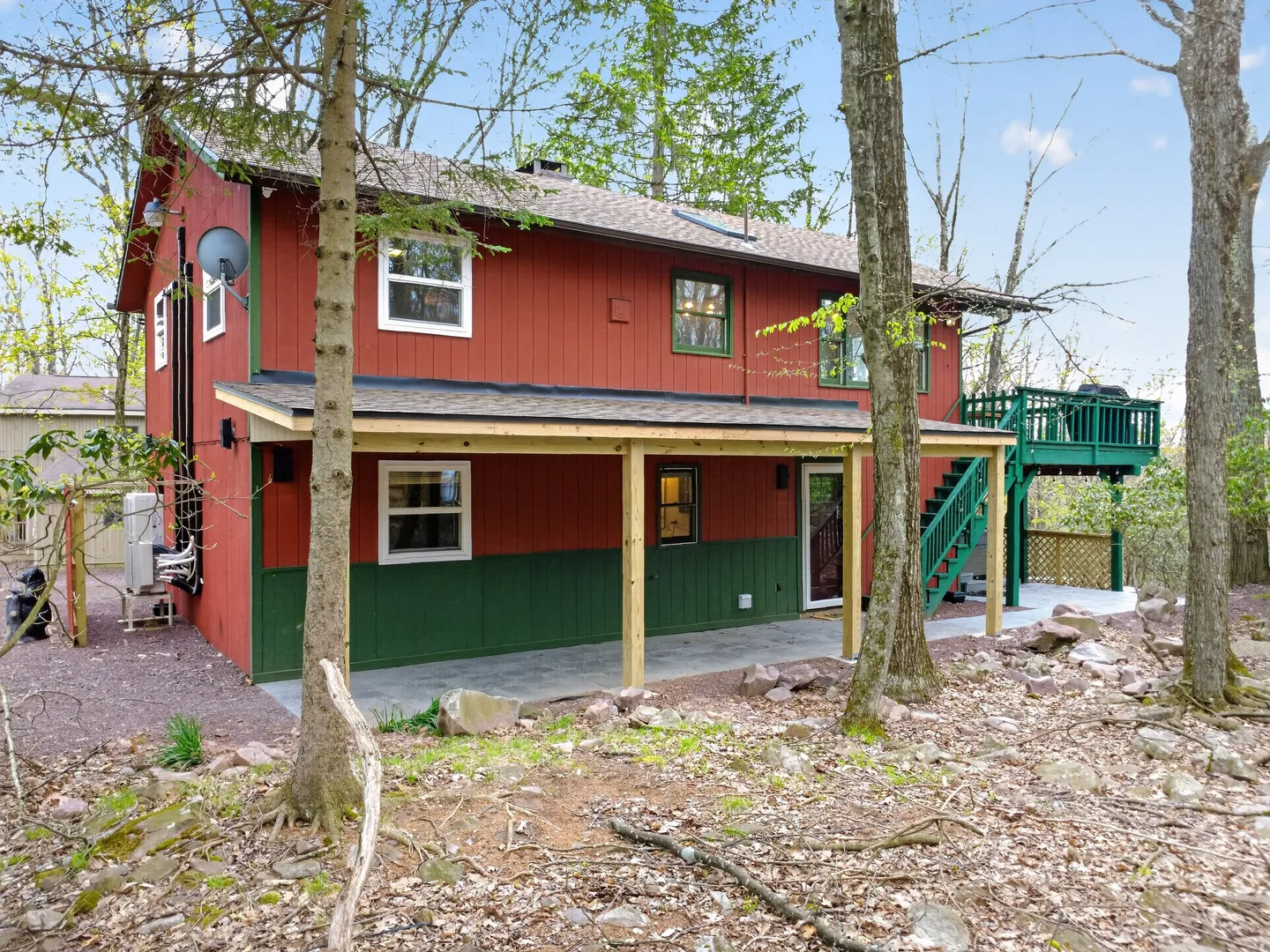 Exterior rear view of a two-story red cabin with green trim, featuring a covered concrete patio and a raised green deck.