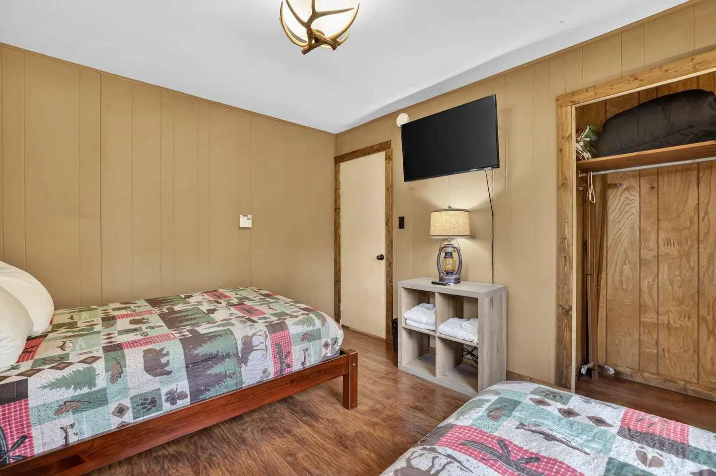 Bedroom featuring wood-paneled walls, two twin beds with rustic patchwork quilts, a wall-mounted TV, and an open closet.