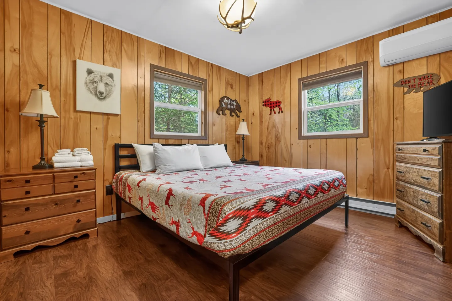 Bedroom with wood-paneled walls, a bed with a patterned quilt, two dressers, and rustic bear decor.