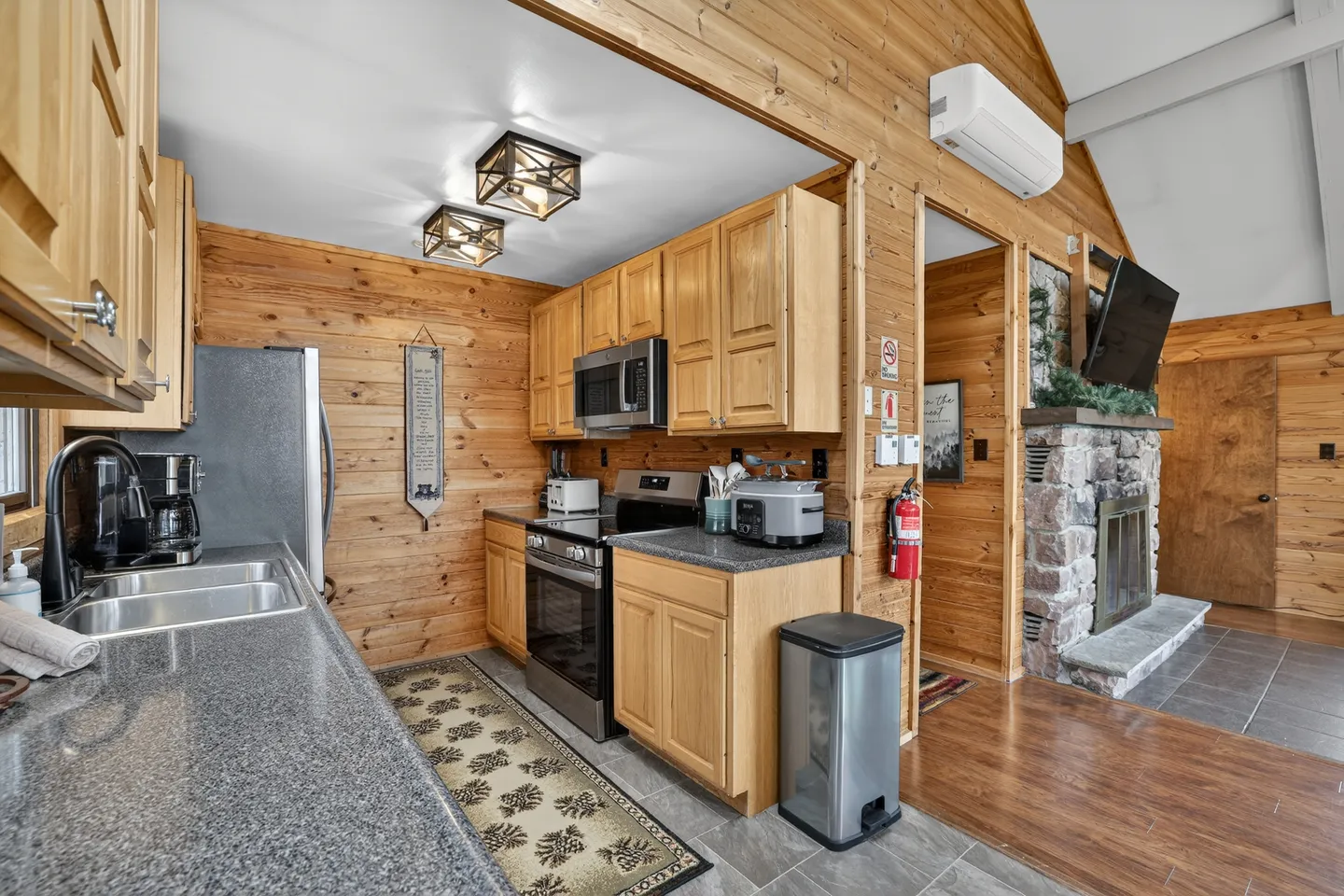 Kitchen in a wood-paneled cabin featuring light wood cabinets, speckled gray countertops, and stainless steel appliances.