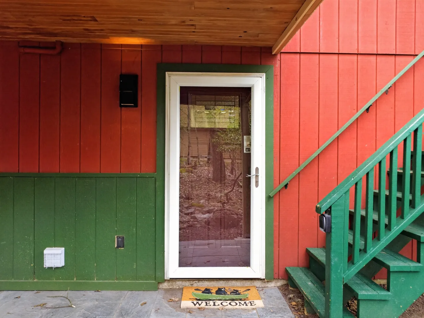 Exterior doorway with a white storm door, red vertical siding, green wainscoting, and green painted wooden steps.