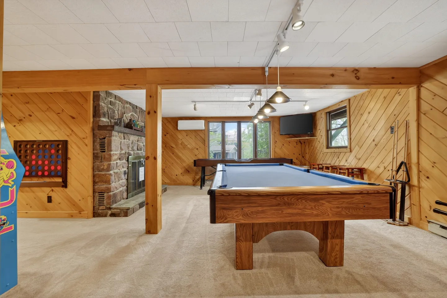 Game room featuring a wooden pool table, foosball table, stone fireplace, and wood-paneled walls.