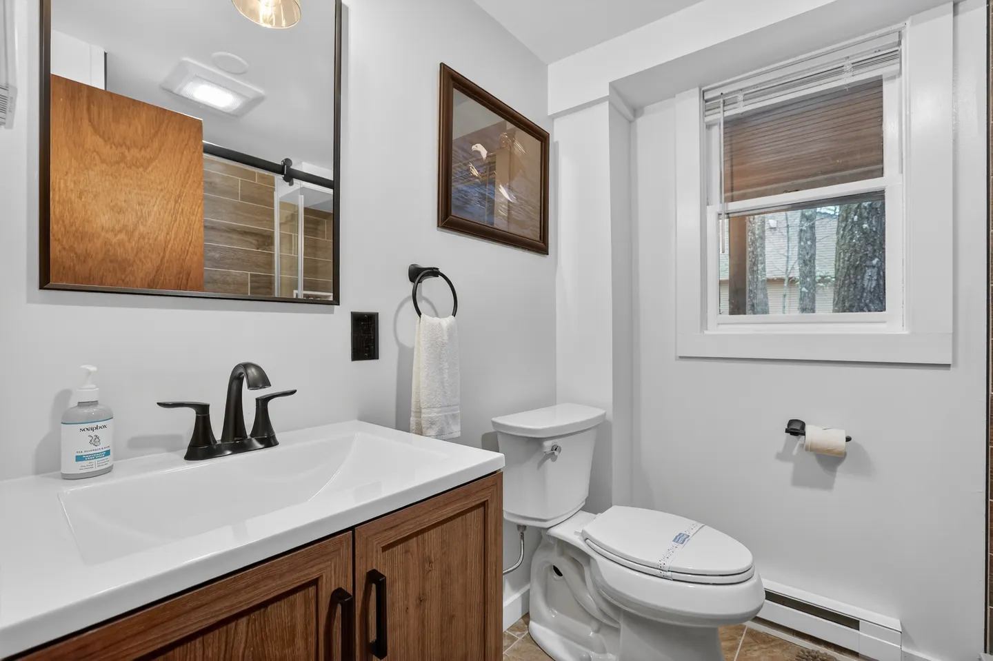 Bathroom with a wood-grain vanity, black fixtures, mirror, toilet, and a window with blinds.