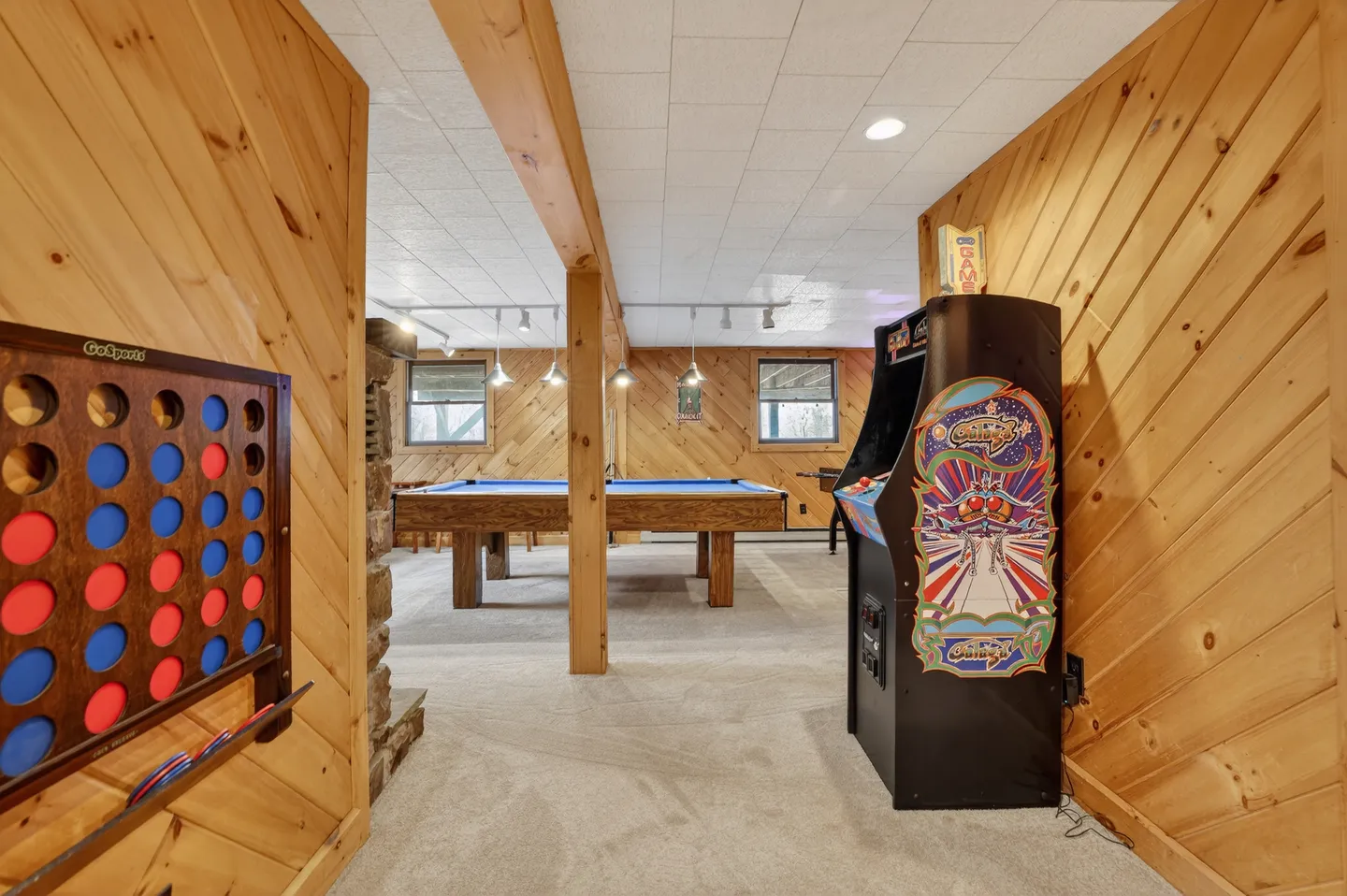 Game room with wood-paneled walls, an arcade cabinet, a pool table, and a wall-mounted four-in-a-row game.
