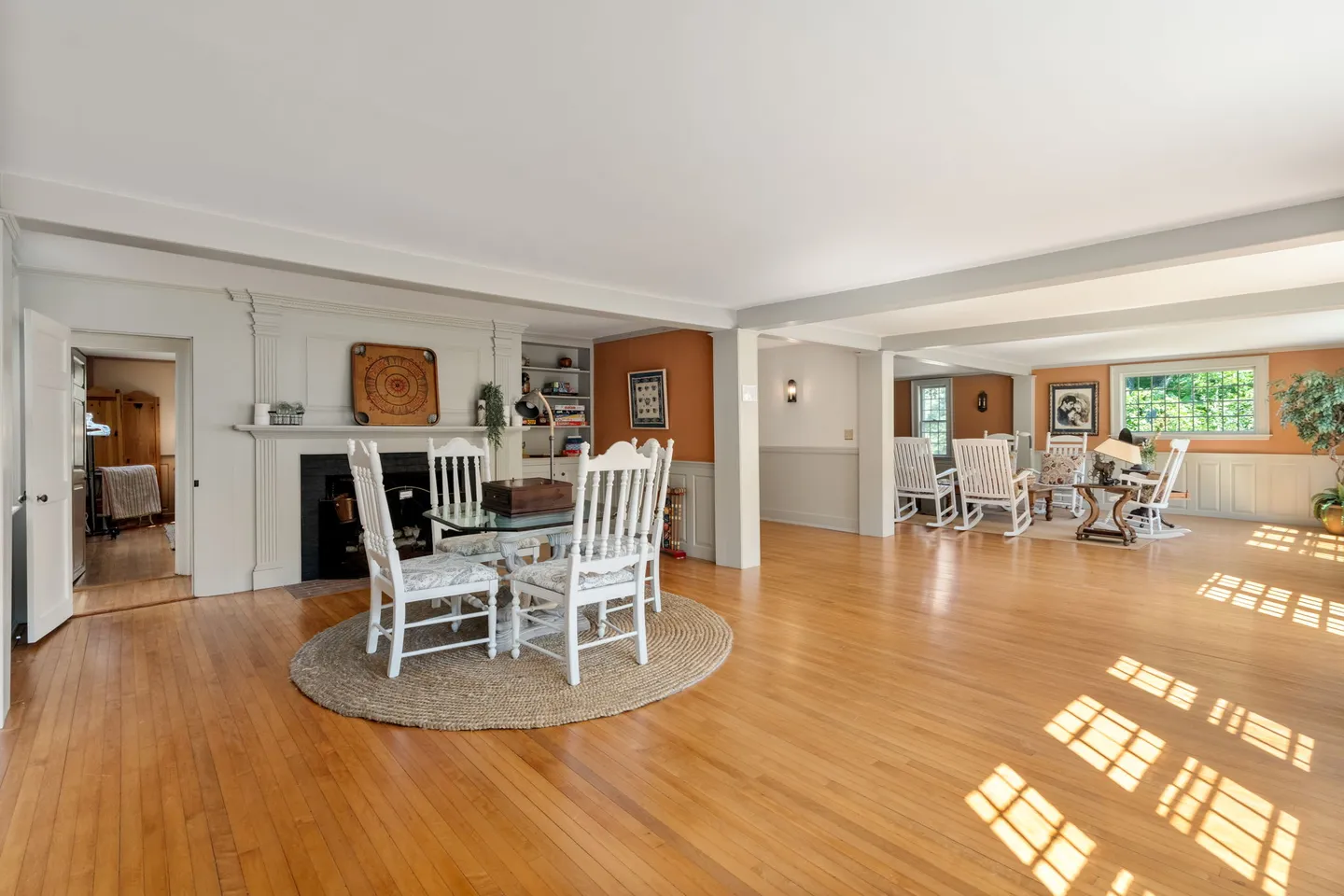 Spacious living area with wood floors, a fireplace, a small dining table set over a circular rug, and a separate sitting area with rocking chairs.