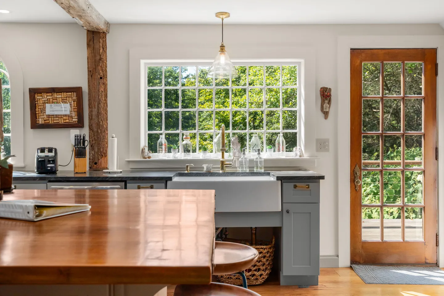 Kitchen featuring a farmhouse sink beneath a multi-pane grid window, wooden island counter, rustic support beam, and a wood back door with glass panes.