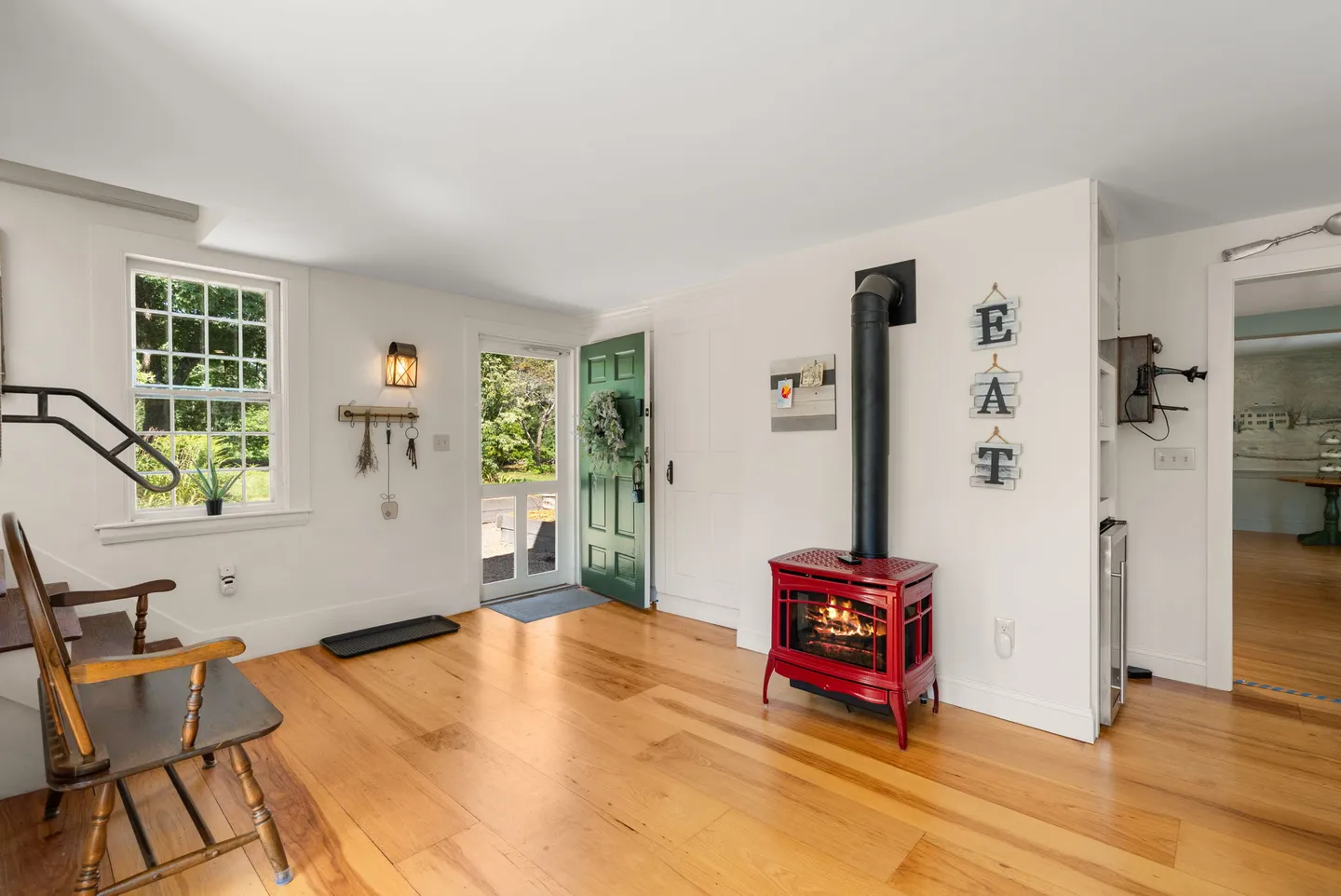 Bright entryway and living space featuring light wood floors, a green front door, and a red freestanding stove.
