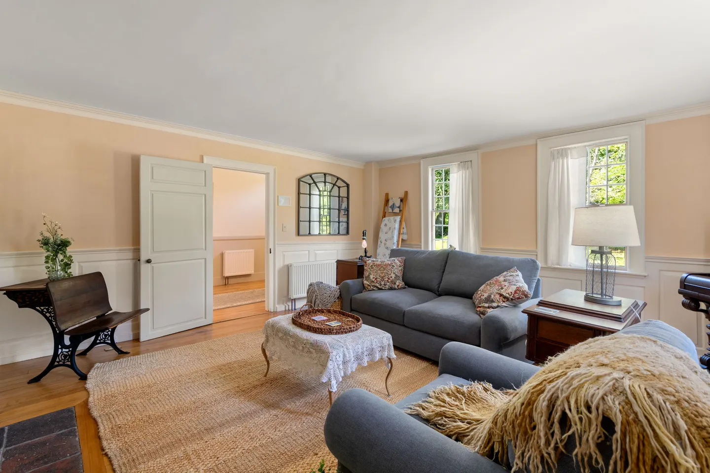Living room with gray upholstered seating, wainscoting, an area rug, and light streaming through two windows.