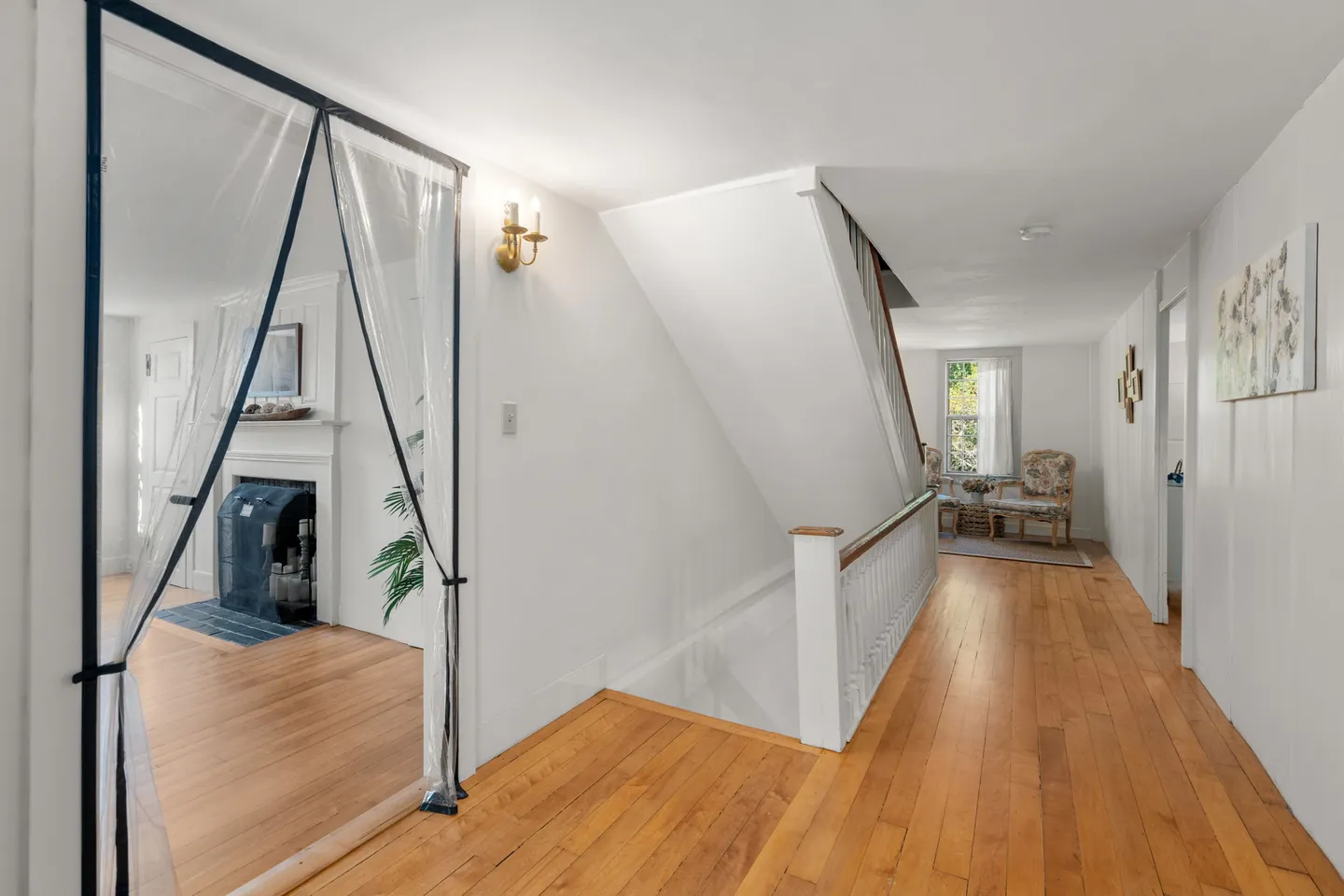 Upstairs hallway with hardwood floors, a staircase with white railings, and an adjacent living room visible through a doorway.