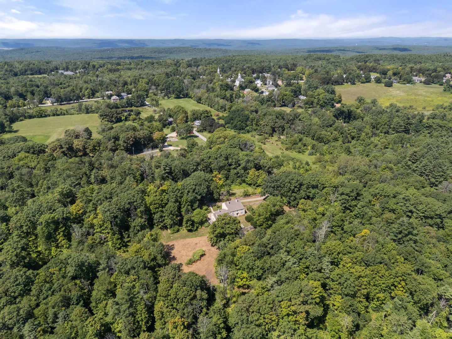 High aerial view of a house nestled in a dense green forest with rolling hills in the distance.