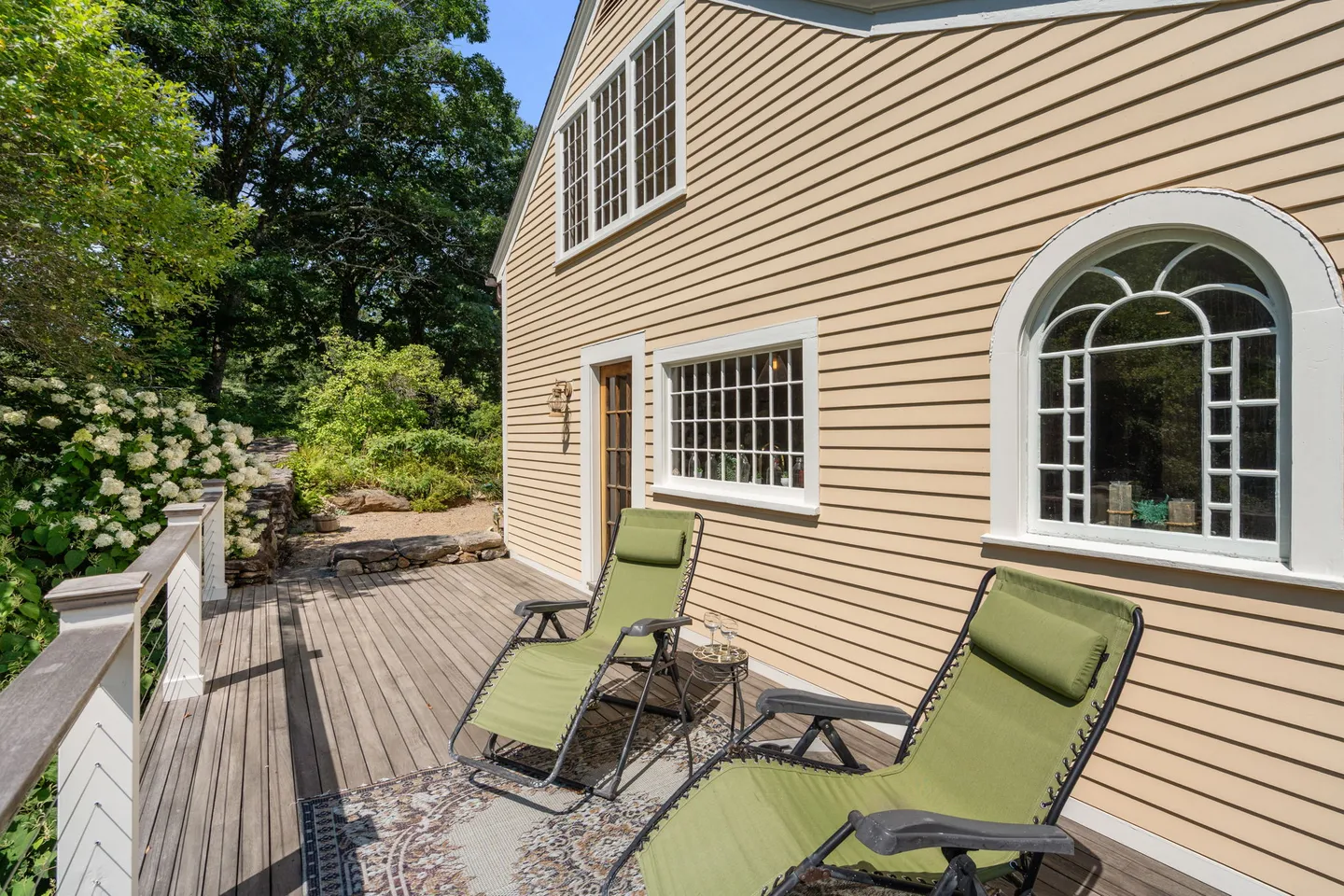 A wooden outdoor deck with two green reclining lounge chairs beside a yellow-sided house with white-trimmed windows.