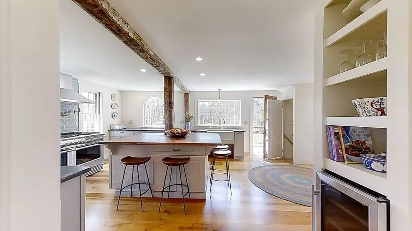 Bright kitchen featuring a central island with stools, exposed wooden beam, and stainless steel range.