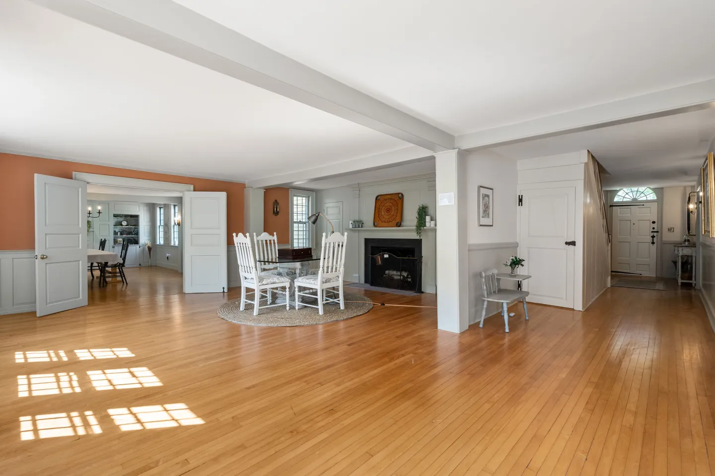 Open-concept interior space with wood floors, exposed ceiling beams, a small dining table with white chairs, and a fireplace.