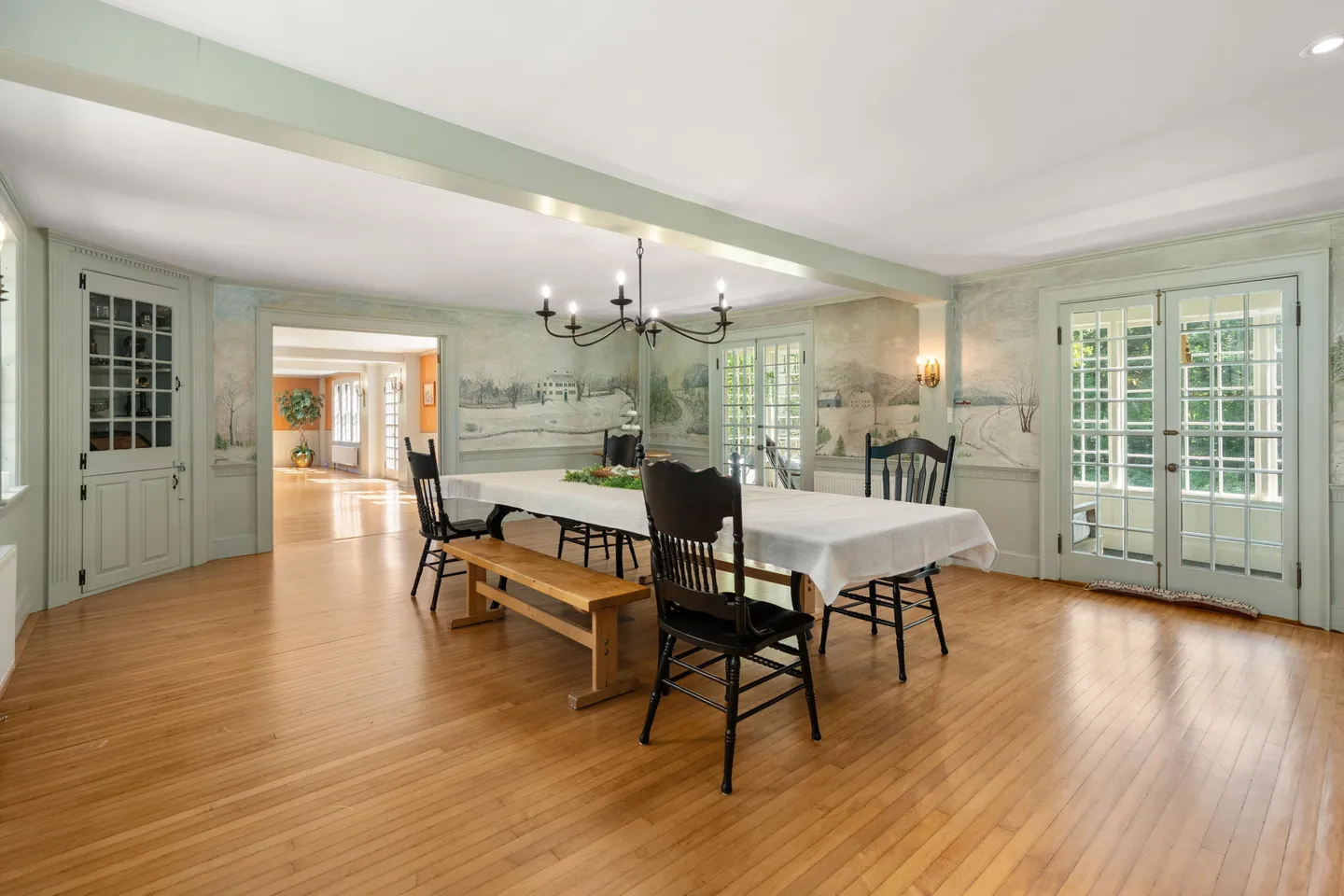 Spacious dining room with scenic wallpaper, hardwood floors, a long dining table, and french doors.