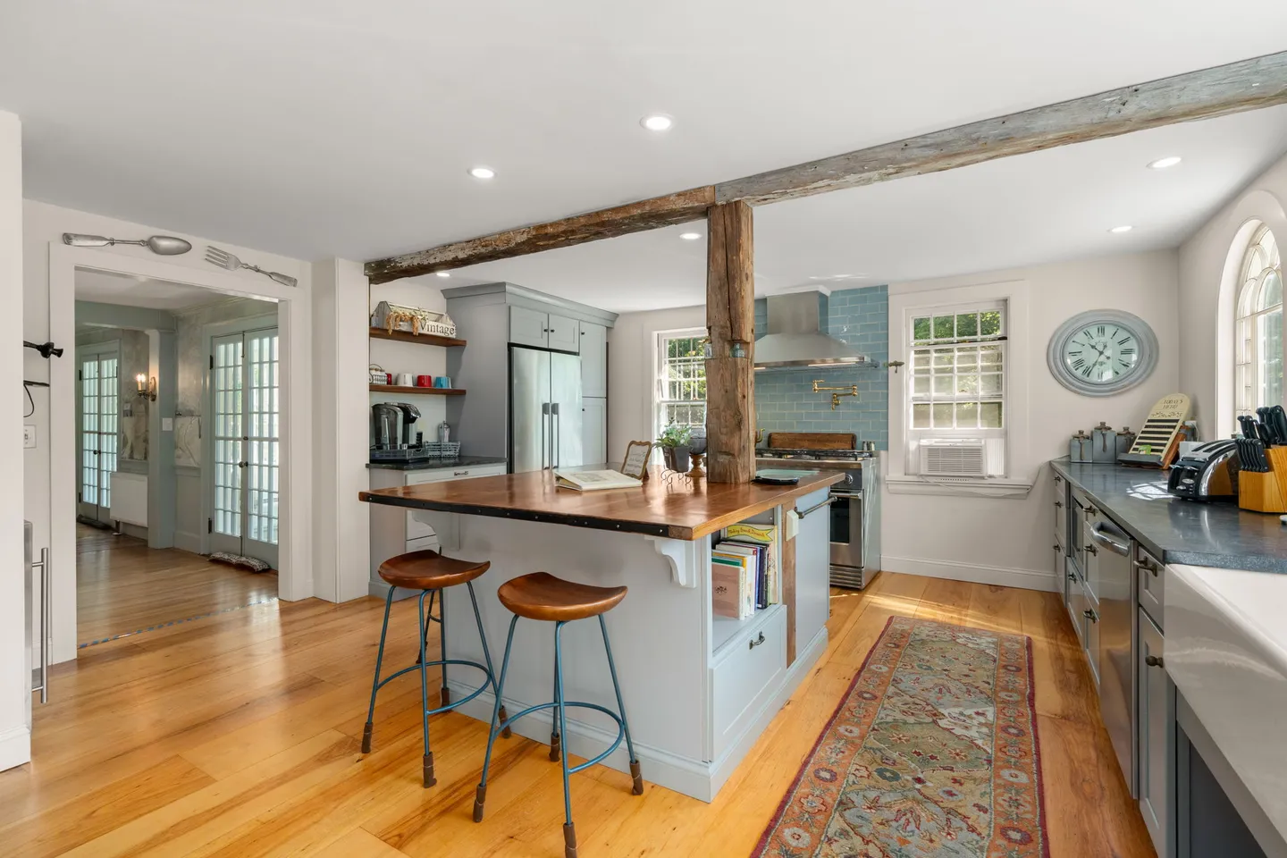 Bright kitchen featuring a wood-topped island with blue-painted cabinetry, barstools, rustic exposed wooden beam and post, and hardwood flooring.