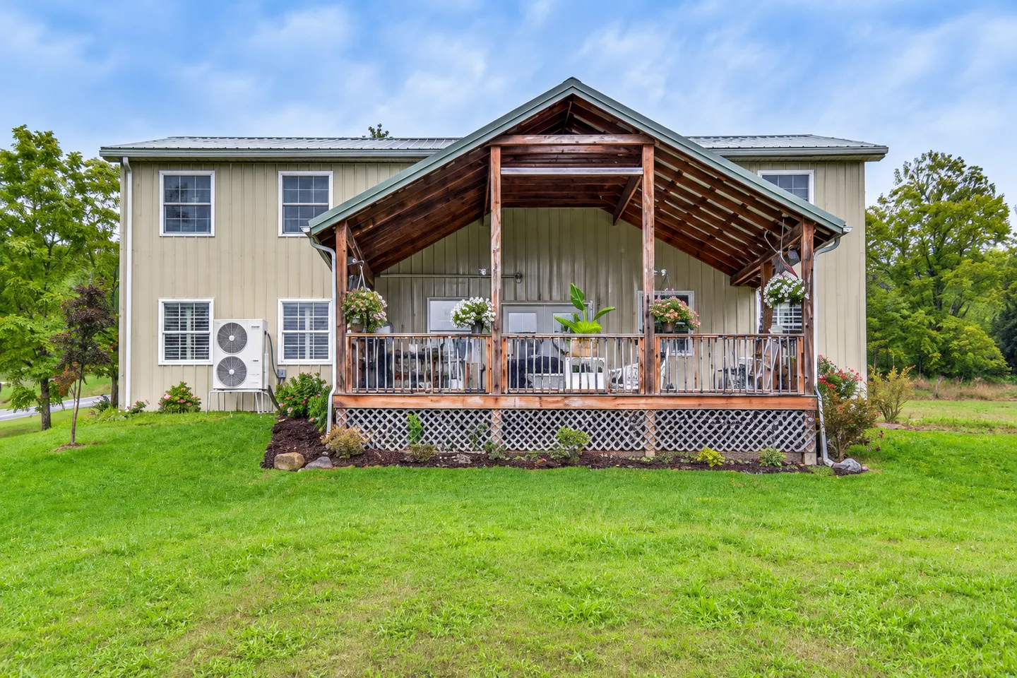 Exterior view of a metal building home with a large covered wooden deck facing a green grass lawn.