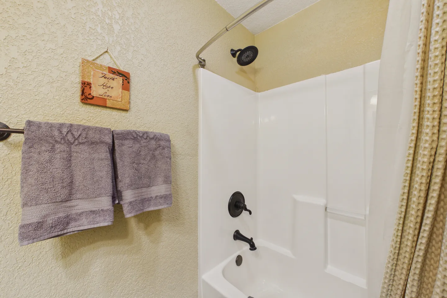 Bathroom showing a white shower and tub combination with dark fixtures, textured walls, and towels hanging on a towel bar.