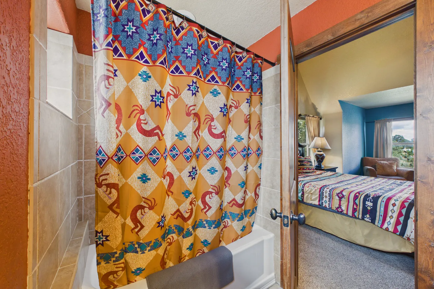 Bathroom view through an open doorway showing a patterned shower curtain and bathtub, with a bedroom visible beyond.