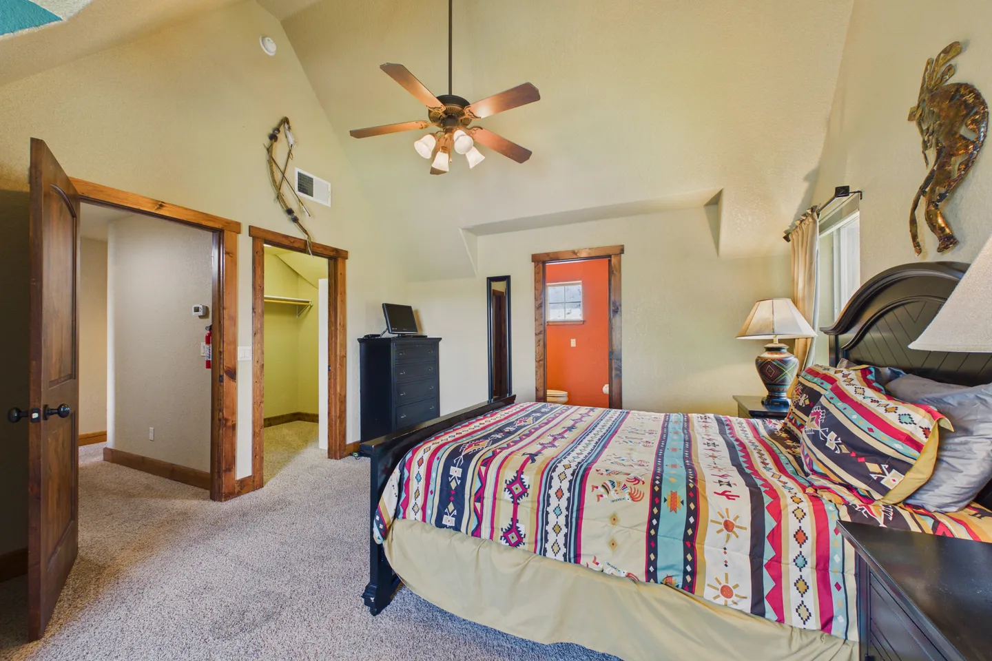 Bedroom with vaulted ceiling, patterned bedding, dark wood furniture, and carpeted flooring.