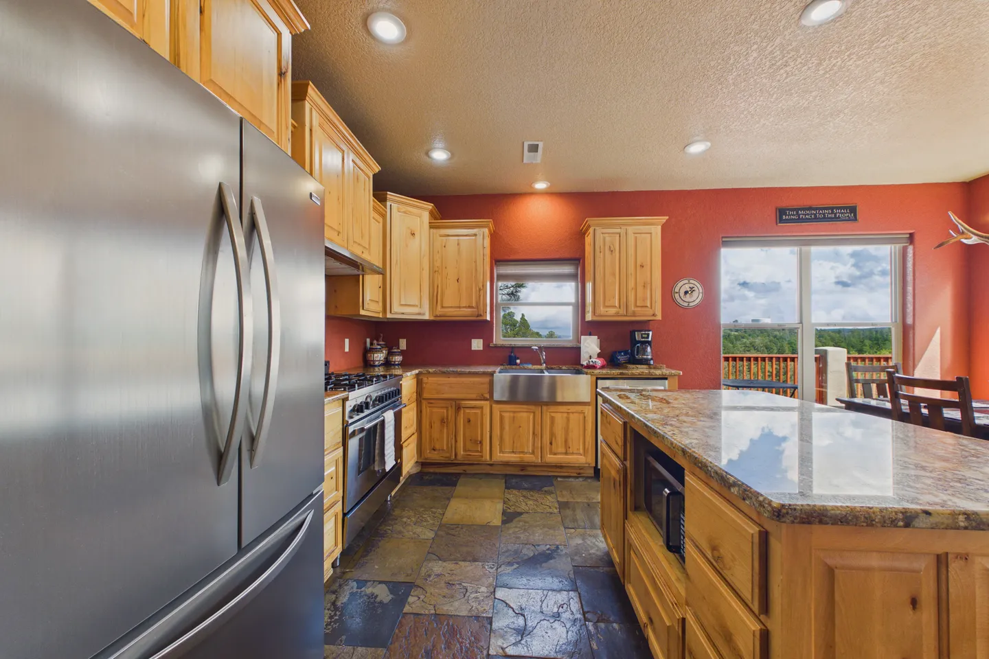 Kitchen with wooden cabinetry, polished granite countertops, stainless steel appliances, and slate tile flooring.