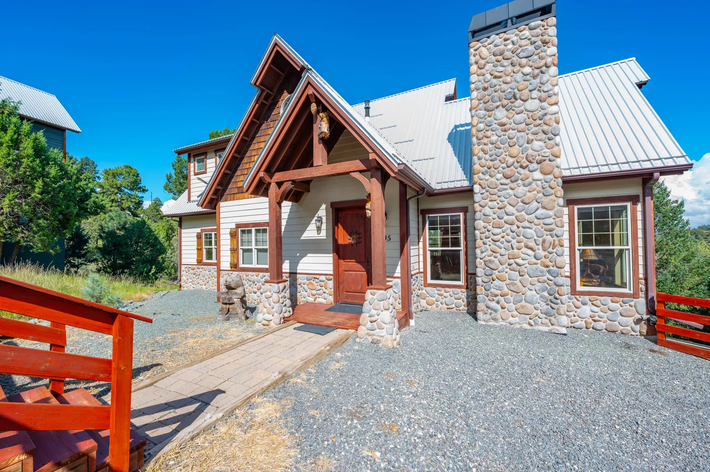Exterior front entry of a mountain-style home featuring stone veneer accents, timber porch, and a metal roof.