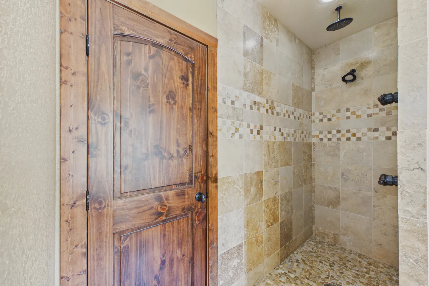A walk-in tiled shower next to a rustic wood-paneled door with a dark knob.