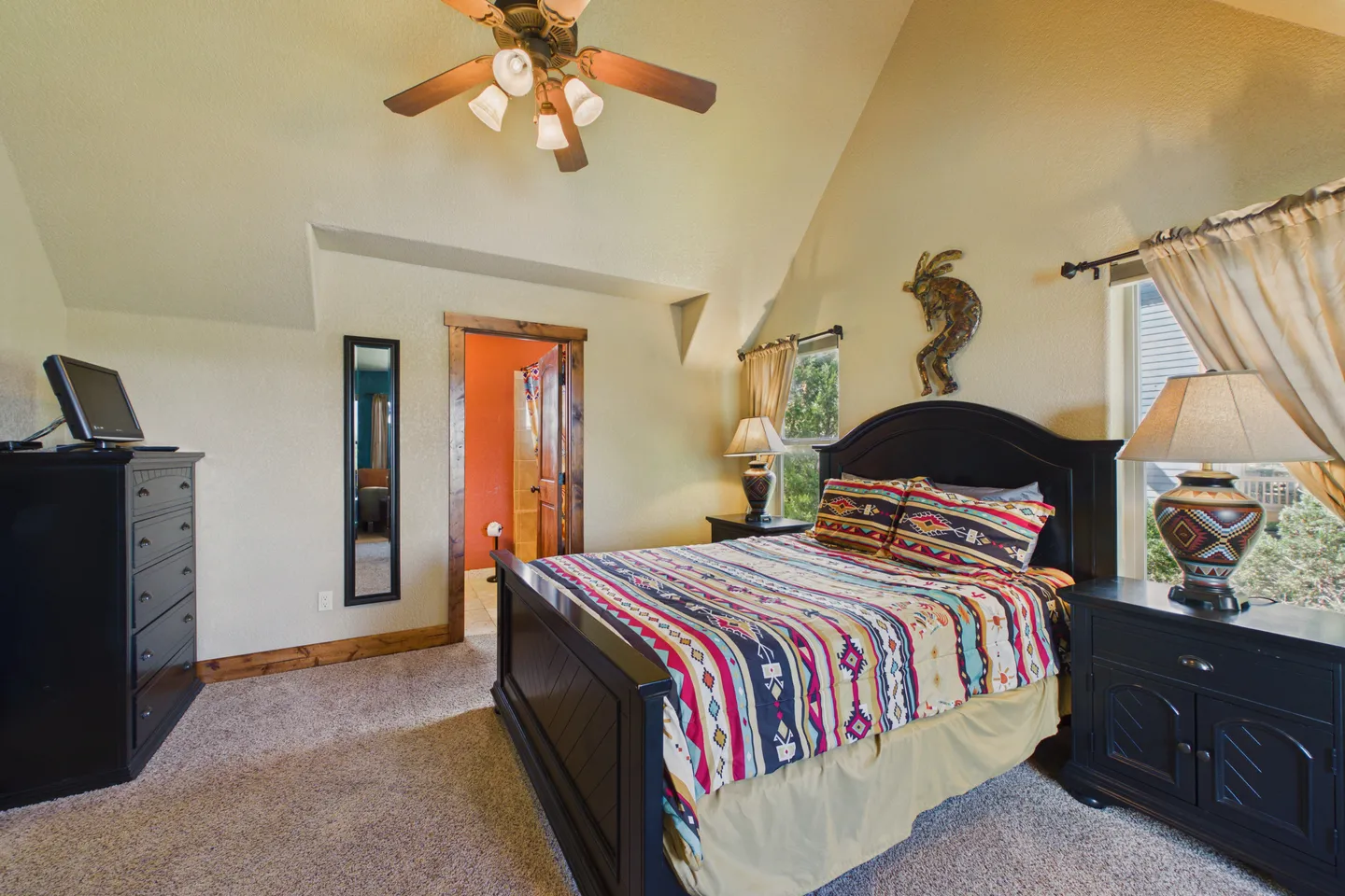 Bedroom with vaulted ceiling, carpeted floor, dark wood bed and furniture, and patterned bedding.