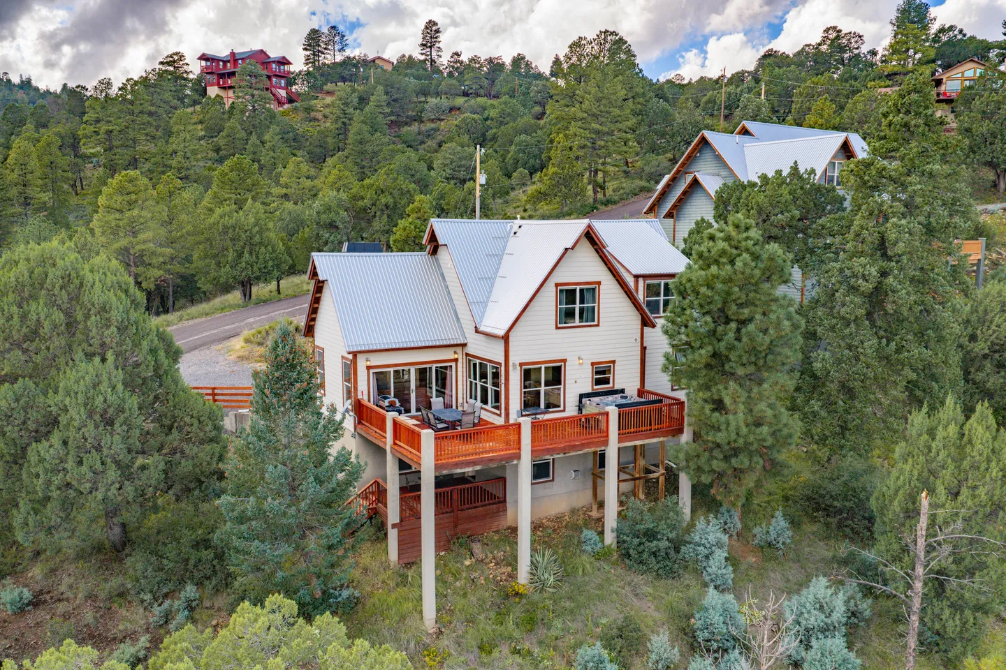 Aerial view of a multi-story cabin with a metal roof and elevated wooden deck set on a forested hillside.