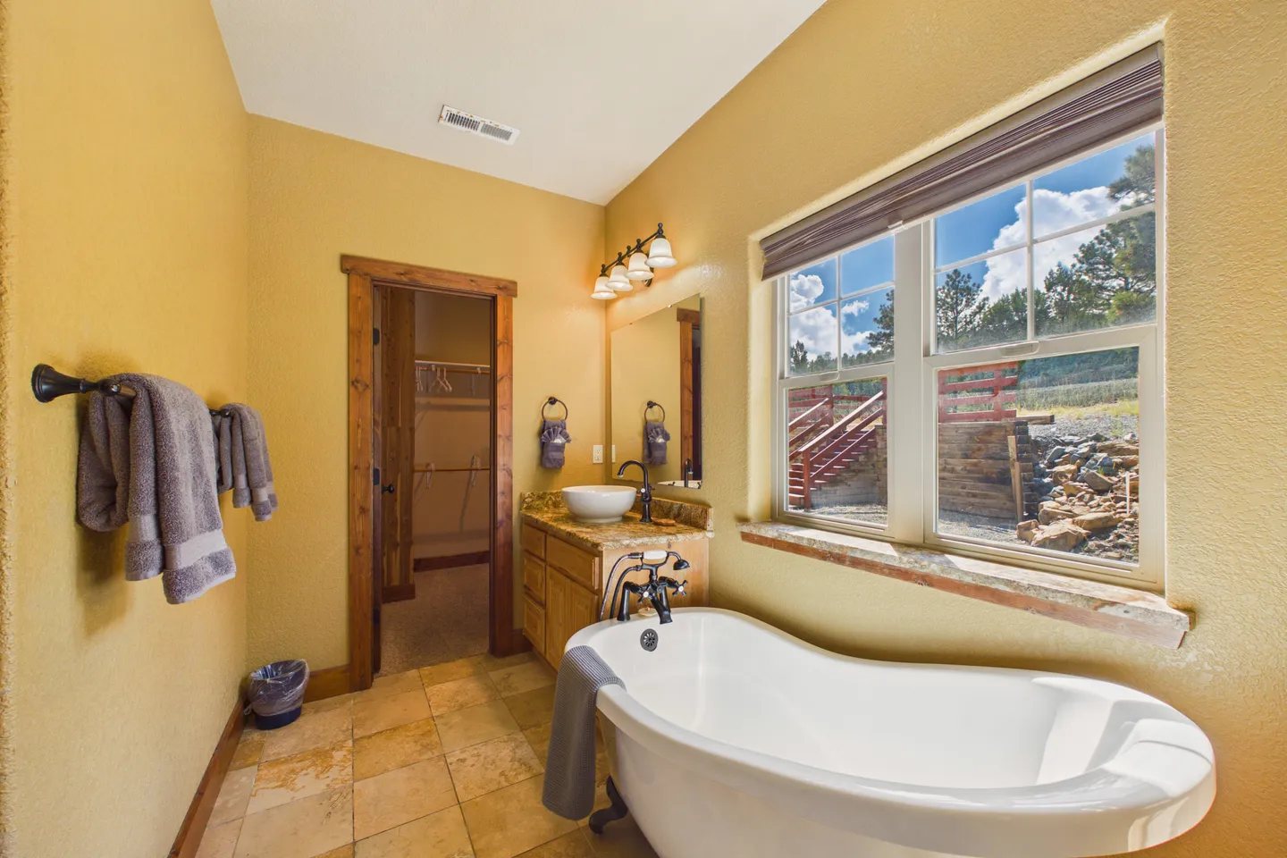 Bathroom with a freestanding soaking tub under a window, a vessel sink vanity, and a doorway leading into a walk-in closet.