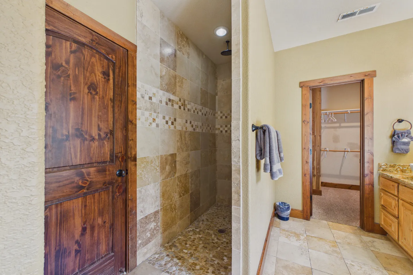 Bathroom showing a walk-in tiled shower, rustic wood door, and doorway leading to a walk-in closet.