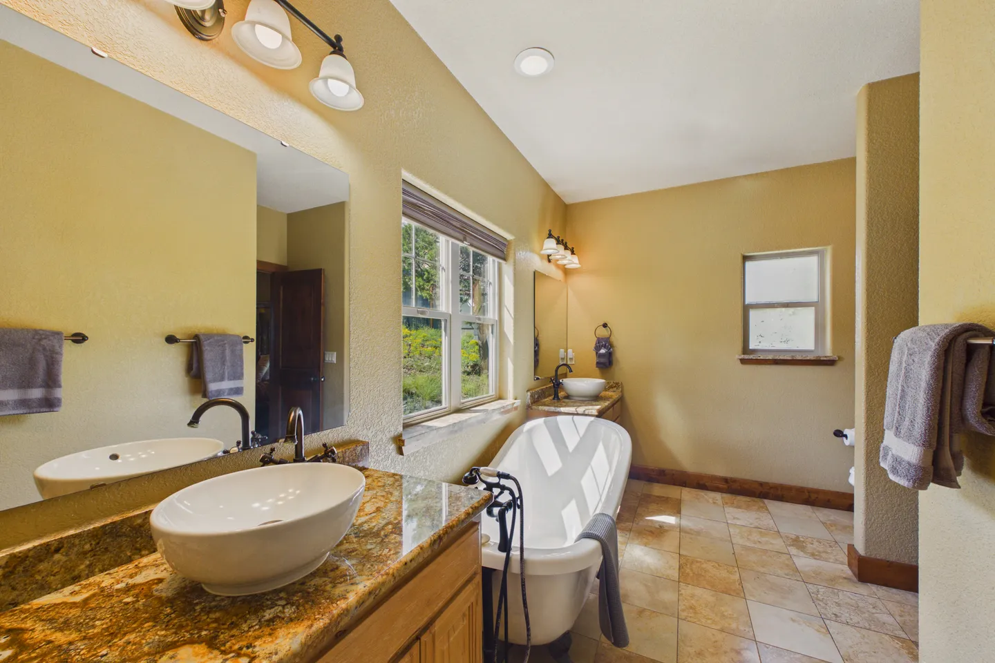 Bathroom with dual vanities, oval vessel sinks, a freestanding clawfoot tub, and warm neutral walls.