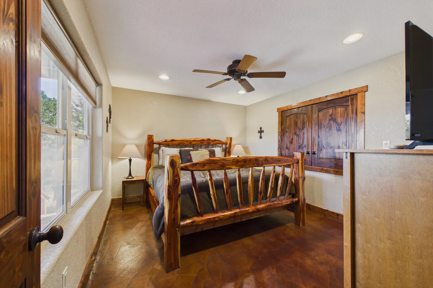 Bedroom featuring a natural wood log-style bed frame, dark stained concrete floors, and a ceiling fan.